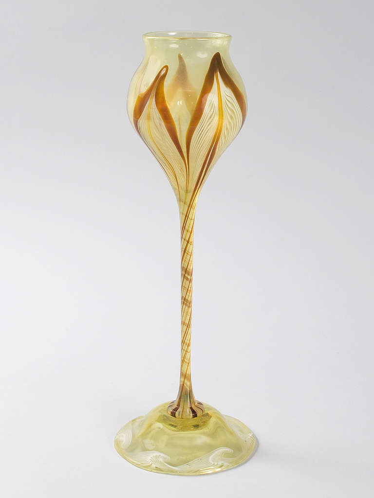 This unique Favrile glass flower form vase from Tiffany Studios New York features a bulbous bowl and elongated internal spiral twisted stem. The vase displays a leaf-like pulled motif outlined in deep orange-red with a white feathered swirl