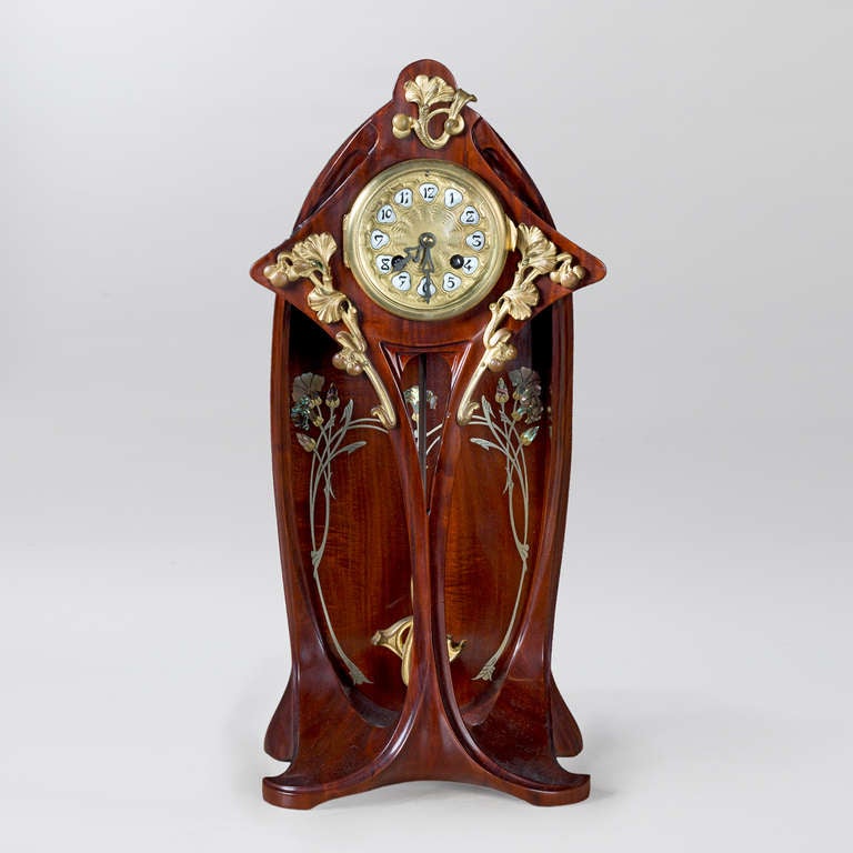 A French Art Nouveau mahogany clock by Georges Ernest Nowak with elaborate bronze, pewter and mother-of-pearl decoration in floral and vegetal motifs. The curvilinear shape of the clock and pendulum are characteristic of the Art Nouveau period and