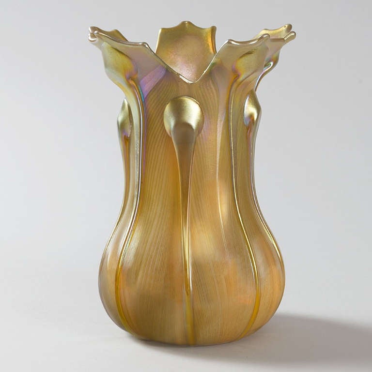 A translucent amber and gold art glass vase by Quezal with overtones of iridescent red and green colors. The vase is enhanced and decorated with ten applied gold glass tendrils which rest upon a pulled feather iridescent ground. The irregular shaped
