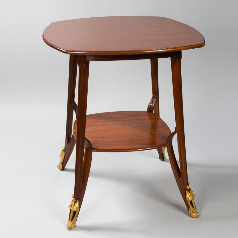 Table carrée à deux niveaux en acajou de Louis Majorelle, de style Art Nouveau français, avec une bordure détaillée sur le niveau supérieur et un plateau en bois.  sabots en bronze doré sur les pieds.    

Une table similaire est illustre?e dans