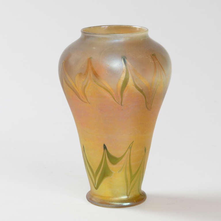 A Tiffany Studios New York iridescent gold Favrile glass vase with iridescent silver and green pulled decoration by Louis Comfort Tiffany. 

Favrile is the trade name Tiffany gave to his blown art glass. The name derives from the Latin word