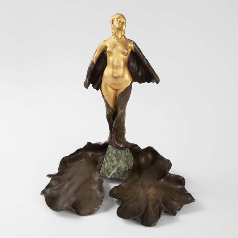 A two toned gilt-bronze and brown patinated figure atop a marble base and tray by Léon-Noël Delagrange. Titled “Unfurling”. Pictured in: Dynamic Beauty: Sculpture of Art Nouveau Paris, by Macklowe Gallery, The Studley Press, 2011, p.