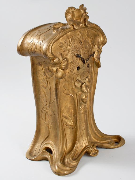 A French Art Nouveau gilt bronze mantel clock by Charles Émile Jonchéry. The curvilinear shape of the clock, as well as the woman’s face in relief below the clock and the decorative flowers, exemplify the Art Nouveau aesthetic. Pictured in: