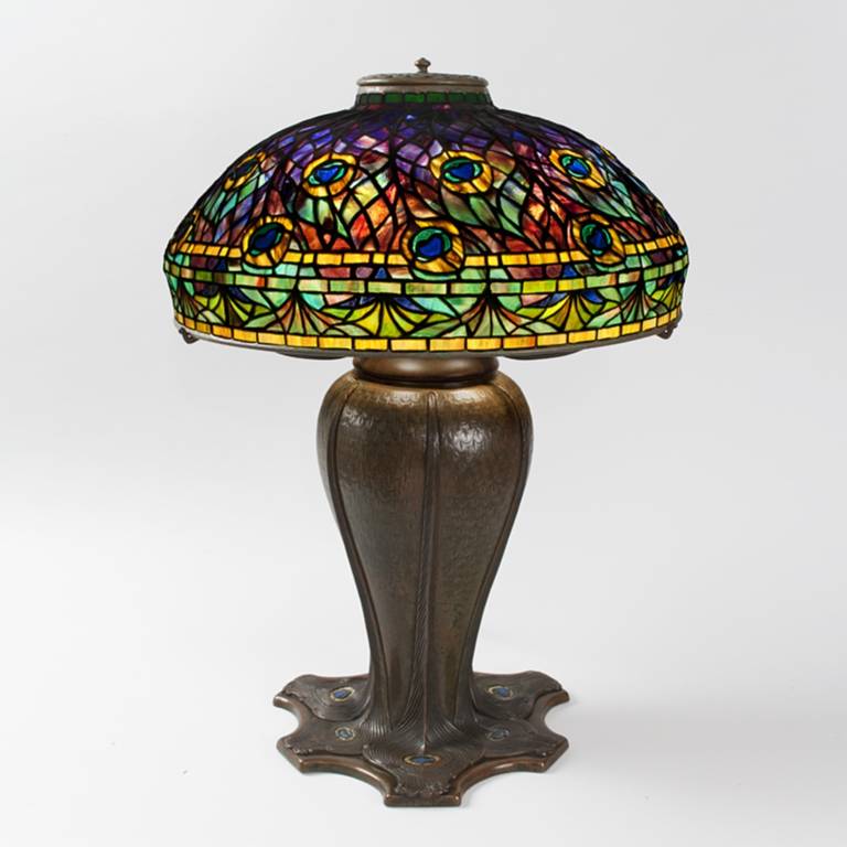 A Tiffany Studios New York Peacock leaded glass and bronze table lamp. The peacock was one of Tiffany’s favorite motifs. Here, brilliantly colored peacock feathers against a rich purple ground create the pattern of the shade with the quills of the