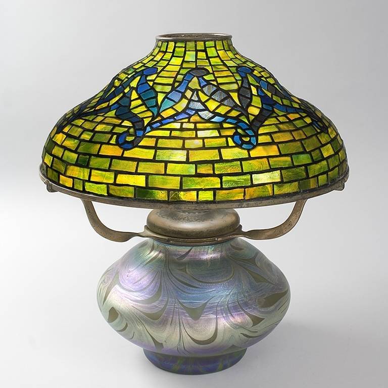 A rare and historically significant Tiffany Studios, New York glass and bronze “Tyler” lamp, the shade featuring an iridescent blue glass decorative pattern on a richly mottled green and yellow glass background. The shade is 16” in diameter, which