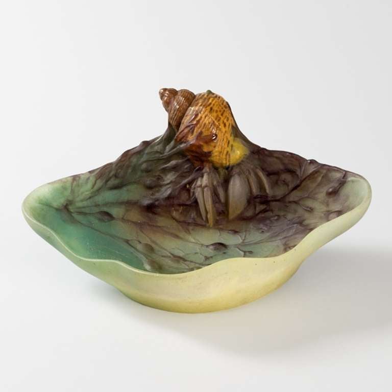 A French Art Nouveau pâte de verre vide poche by Amalric Walter. The piece features a hermit crab with brown and yellow shell and green claws perched atop a bed of seaweed and surrounded by light blue watery ground.

A similar vide poche is