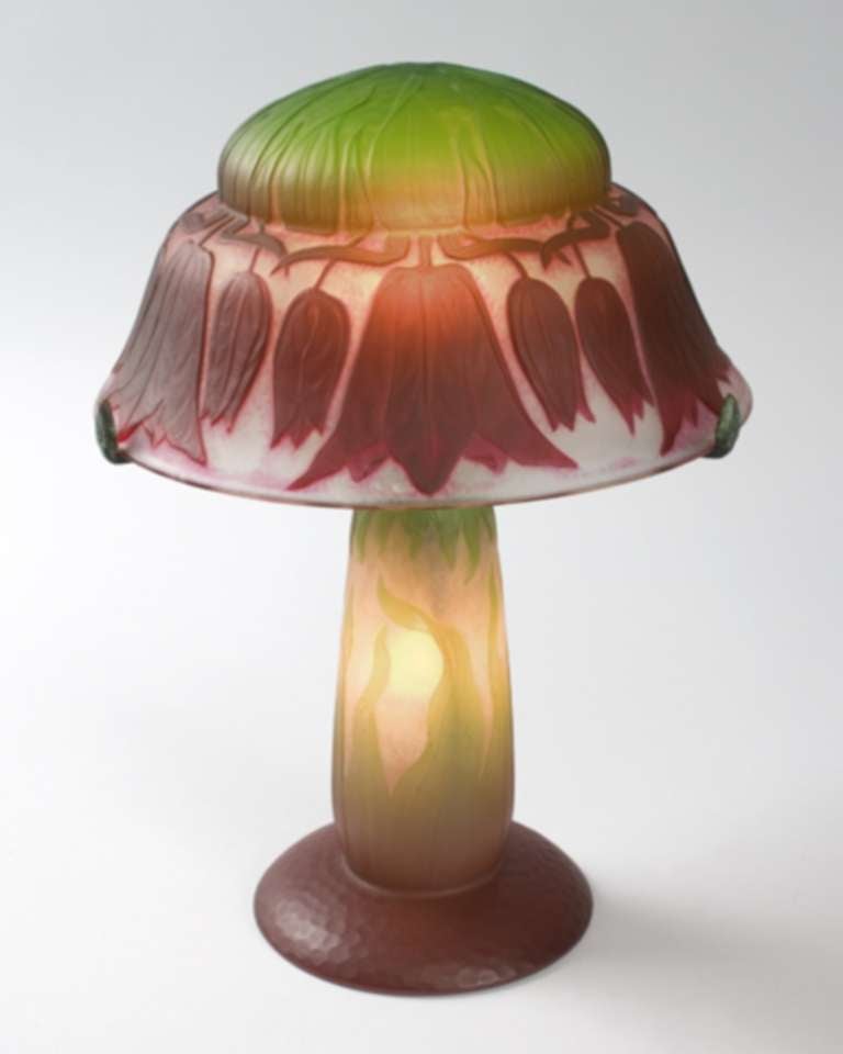 A French Art Nouveau cameo glass table lamp by Daum, featuring bright red flowers on an opaque white and cream ground. The top of the lamp is in a bright green hue. Circa 1900.

Signed, 