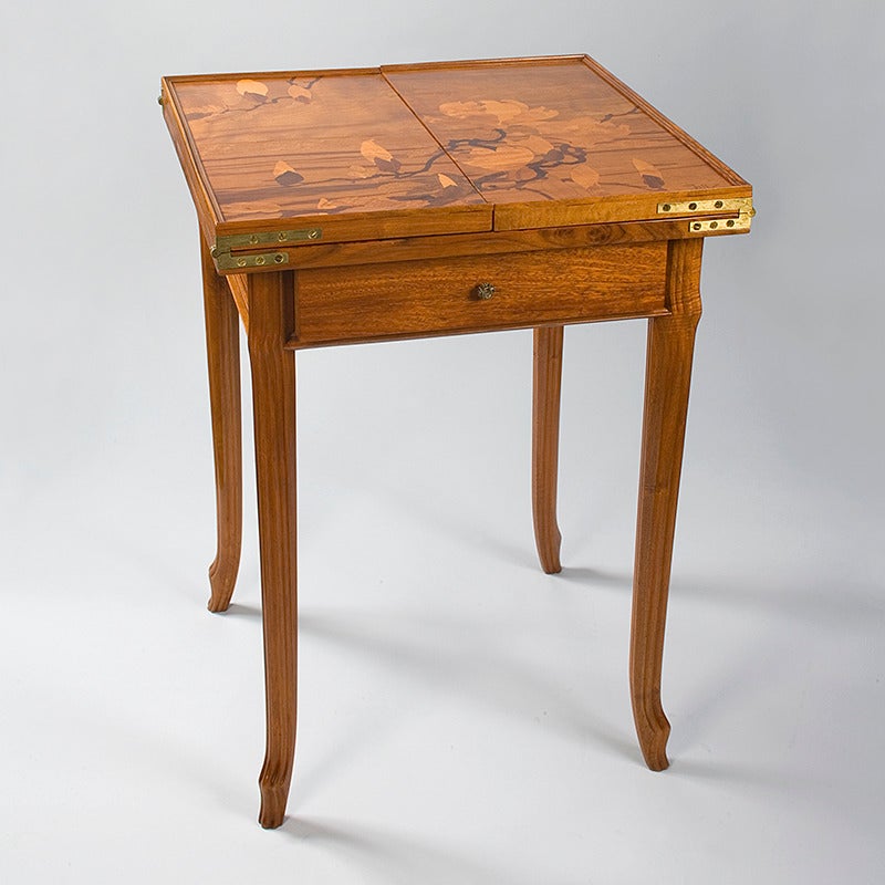 A French Art Nouveau games table in cedar and walnut by Emile Gallé, featuring inlaid marquetry when closed and open. When closed, the marquetry decoration is of tree branches with buds and flowers and can serve as an end table. Opened, the motif is