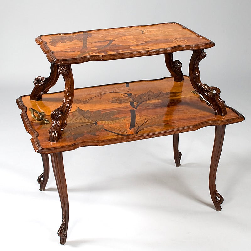 A French Art Nouveau two-tier table by Emile Gallé, featuring inlaid marquetry depicting a natural landscape in a combination of rosewood, walnut and fruitwoods. The table is further complemented by bronze handles, cast to represent stylized