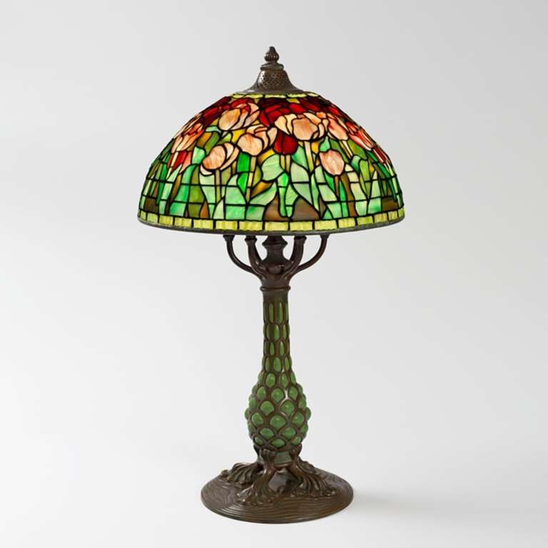 Tiffany Studios “Tulip” table lamp with pink and red flowers on a blue and green ground, accented by two bands of glass, blue at the top and green at the bottom of the shade, respectively. The shade sits atop a four footed bronze 