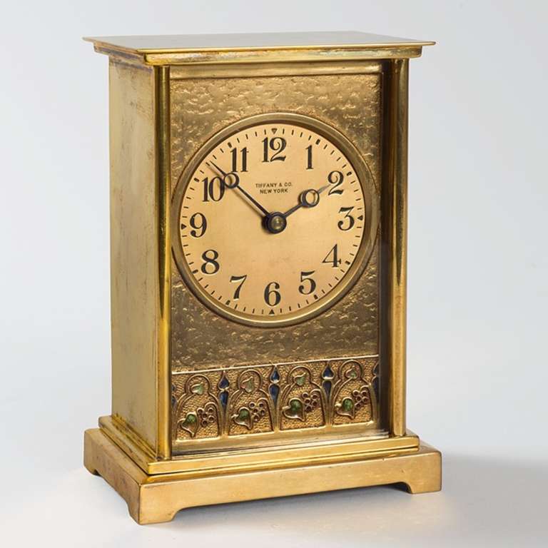 A Tiffany Studios New York American Art Nouveau gilt bronze clock by Louis Comfort Tiffany.  The rectangular clock is decorated at the bottom with green and blue enamel stylized blossoms, stems and leaves. Circa 1900.

Signed, 