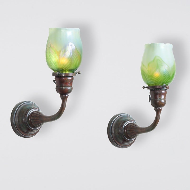 A pair of Tiffany Studios New York single arm wall sconces with green iridescent tulip shades with pulled decoration  A similar sconce is pictured in: Alastair Duncan, Tiffany Lamps and Metalware: An illustrated reference to over 2000 models,