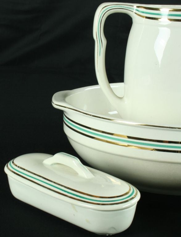 A five-piece Art Deco Vanity Set, including Bowl, Pitcher, Chamber Pot, Jewelry Dish, and Comb Dish, in ceramic with green and gold striping in the Henriette pattern and marked with the Nimy signature