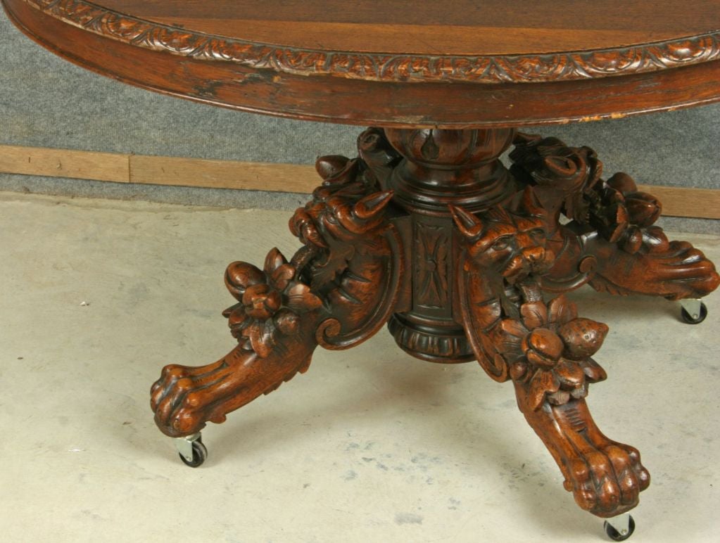 An oval Hunting-style Dining Pedestal Table from France dating to 1880 in oak with a nice patina and heavily carved legs featuring stylized lions, fruit, and claw feet.