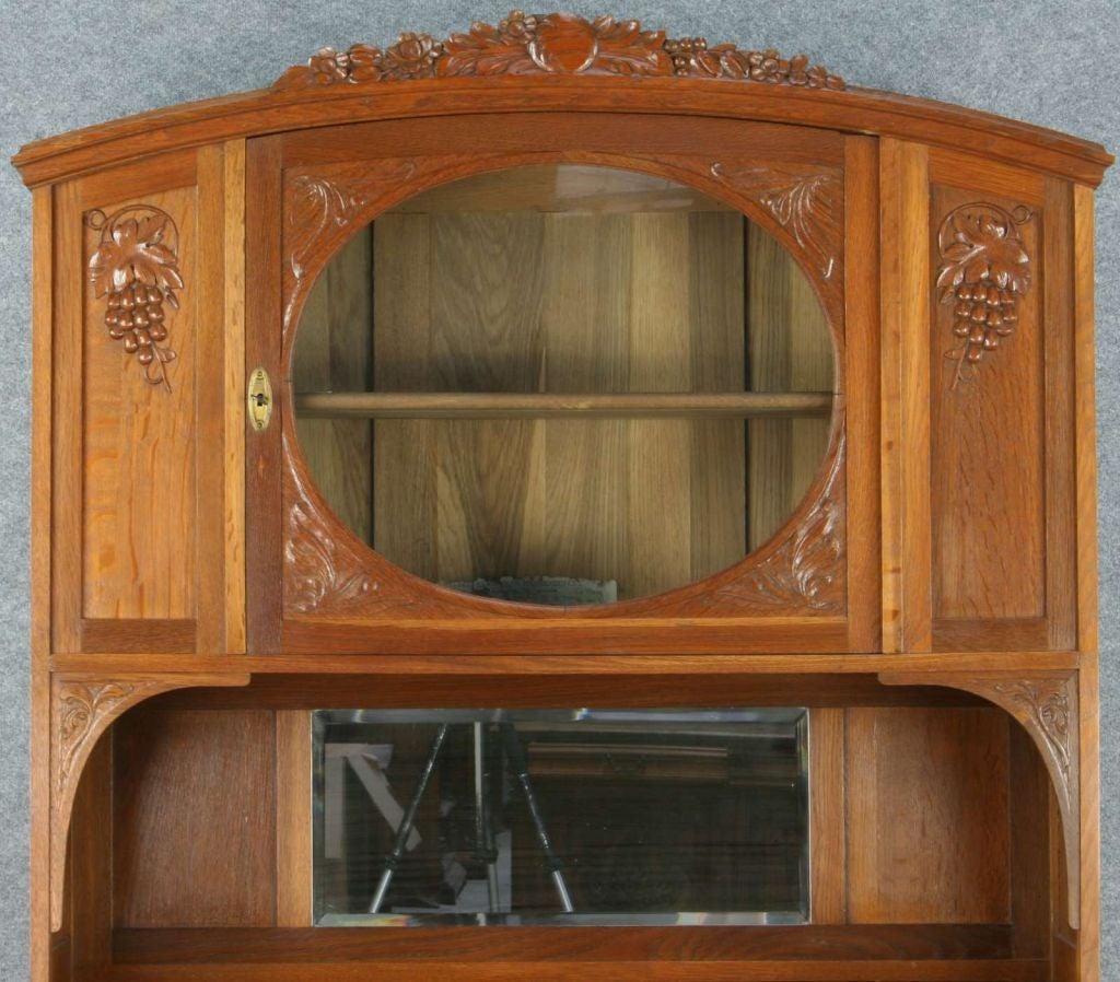 An Art Deco Buffet Server China Cabinet from France dating to 1920 in oak with charming carved grapes and an interesting round glass central door.