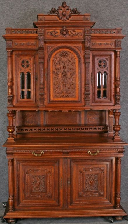 A large Renaissance-style Buffet Server China Cabinet Hutch from France dating to 1900 in oak with beautiful carved flourishes and upper doors in a Gothic motif