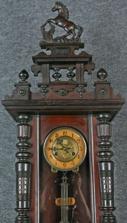 An exceptional German Regulator Wall Clock in the Viennese style dating to 1890 with a mahogany case featuring turned and carved columns and topped by a rearing horse. The embossed brass dial and pendulum are quite attractive.