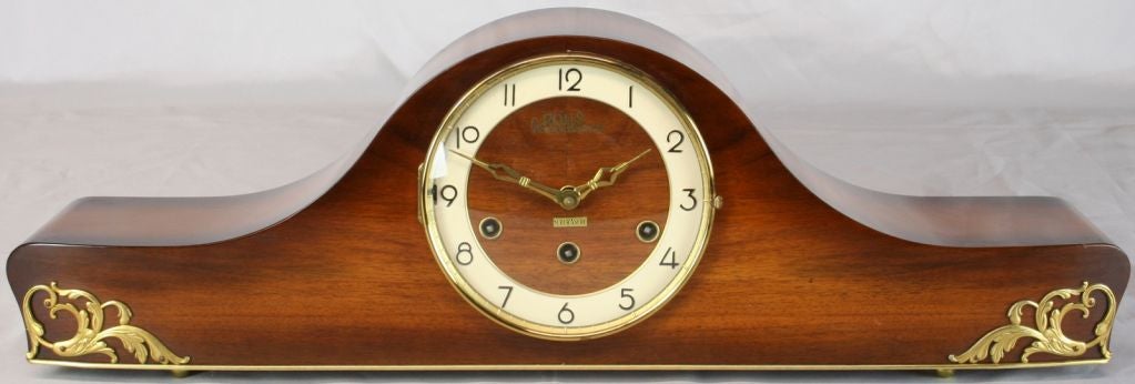A German Mid-Century Modern Mantel Clock with a mahogany and brass case and marked Rols Super Ancre. The clock is in running condition and plays the Westminster chime.