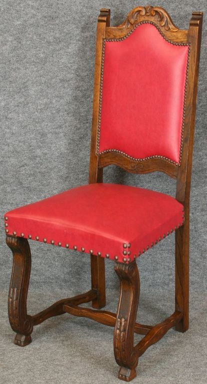 A Set of 6 Renaissance Style Dining Chairs from France dating to 1950 in oak with red leather-like upholstery and featuring carved backs and shapely legs.