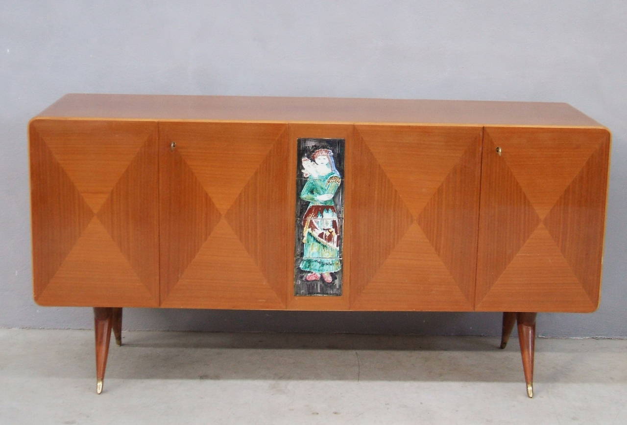 1940s Art Deco four-door Italian sideboard with centered signed ceramic artwork. 
Featuring 2 shelves behind the middle doors and has the original angled tapered legs with Brass Sabots.
The Credenza is in original good condition with wear and tear