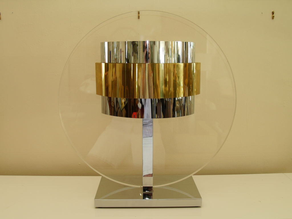 The lamp has a large round lucite panel with chrome and brass details on each side. This is an oversized table lamp with simple lines to make a grand statement.