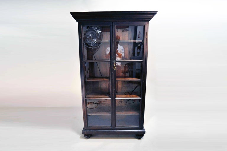 This freestanding bookcase from India was made from teak wood by native craftsman in the British style.  Teak bookcases protected books and ledgers from tropical insects and dust. There are 10 glass windows, bun feet and a stately crown molding to