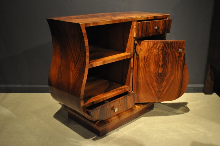 This stylish Art deco side chest has an elegant curvaceous figure. The chest features open and closed storage in an asymmetrical pattern. The walnut veneer is in wonderful condition. 
