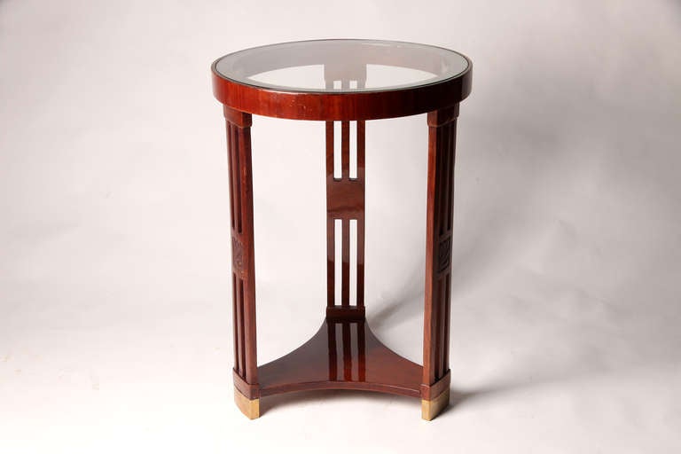 This elegant Hungarian round table features three decorative legs and a glass top. It is from Budapest and is made from mahogany veneer.