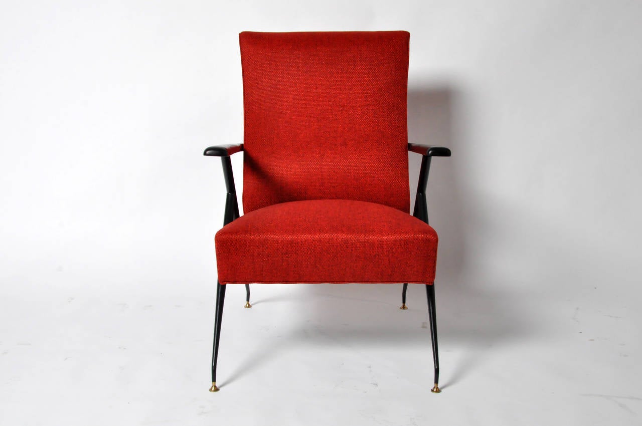 This bold and transformative pair was recently reupholstered in a rich red fabric. Raised on elegant A-frames, the cylindrical tapered legs terminate in brass-capped feet. Ready to relax? With a simple lift, each of the lacquered elmwood arms swing