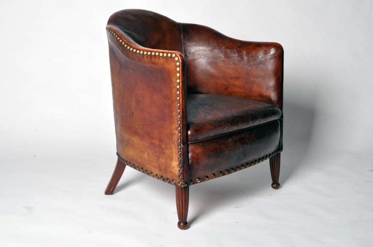 This graceful and richly aged leather club chair features fluted wooded feet, a scalloped back and brass nail heads. 