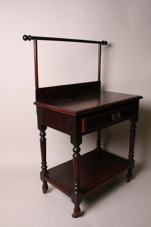 A British officer likely used this petite washstand in his private quarters; the top rail—used for draping clothes or towels—is raised above a central tabletop with a large drawer below which the turned legs are joined by a secondary shelf and