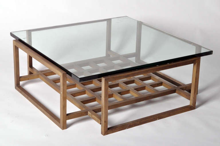 This Mid-Century Modern low table is a handsome convergence of both materials and shapes. Pulling from the Hollywood Regency style of mixed metal and glass, the thick cut translucent top surmounts the grate-form base. While squares are a primary