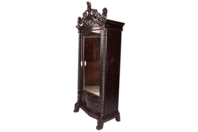 Handsome carved details throughout this piece on serve to elevate its stateliness, the openwork floral motif cornice is topped and flanked by decorative peacock-form finials. The mirrored central door that conceals two shelves and drawers is framed