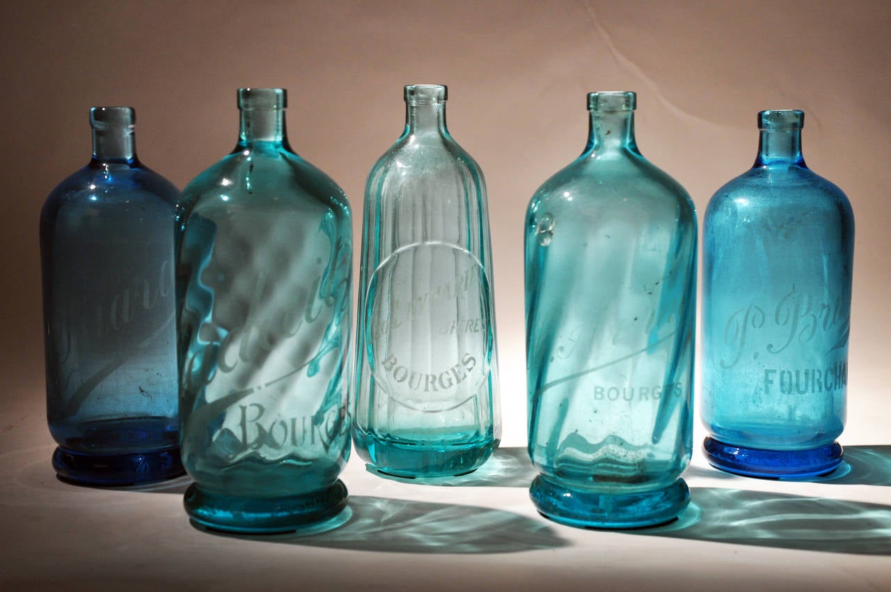 Our collection of seltzer bottles conjures up the glamour of pre-war French cocktail culture. The bottles once came in a variety of colors with blue being the most common. Each bottle bears the etched logo of a company that bottled naturally