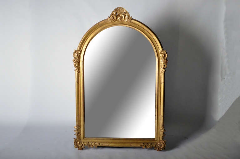 The large arched rectangular mirror plate is framed by intricately carved Rococo motifs. Swirling C-scrolls flank the shoulders, shell or rocaille form crests with flowering branches are carved in each lower corner and both designs intertwine to