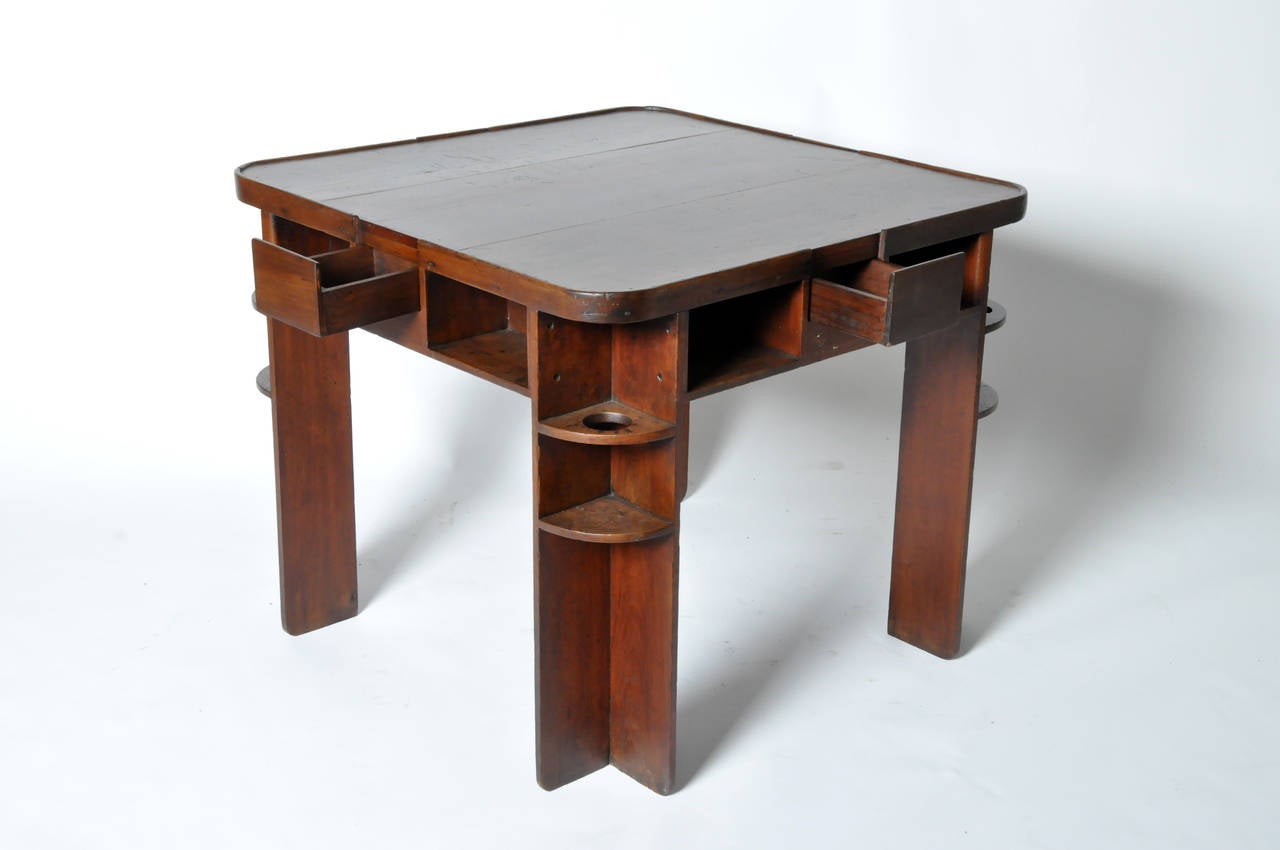 This Classic game table features a rosewood top and teakwood frame. The surface has a surrounding lip to keep dice from falling off. There are four drawers for storage, and a drink holder on each leg--where small burn marks elude to past resting