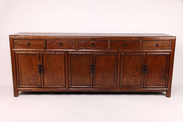 This Elm Wood sideboard features five drawers, raised above additional storage compartments. Removable shelves in each compartment are concealed by three pairs of doors with metal lock plates. No nails were used in the construction of this piece; it
