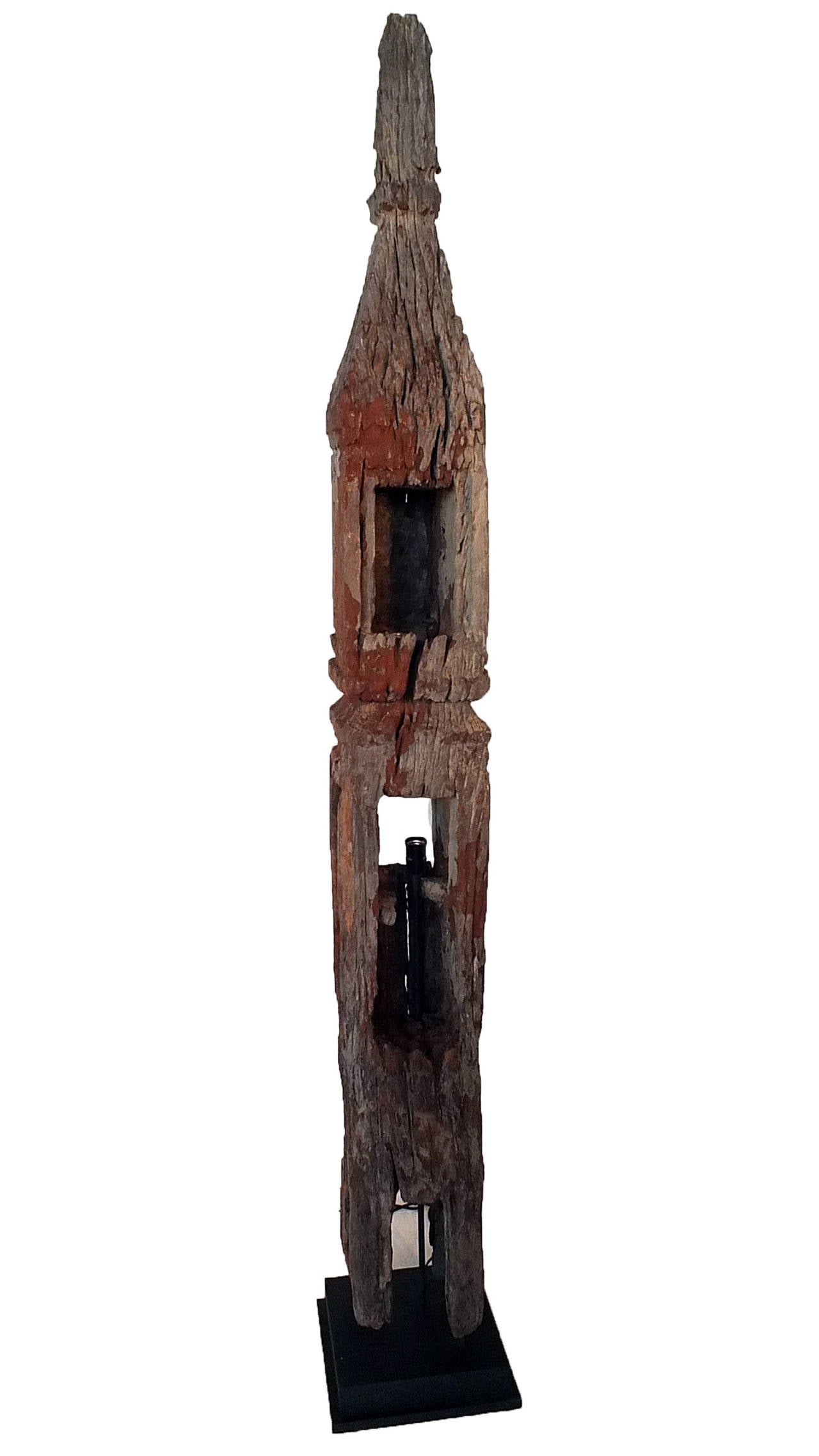 The pointed spire is raised above a square pillar with multiple carved niches, of which the middle has been retrofitted as a lamp. Remnants of the original paint have since weathered and faded to a rust-like color.