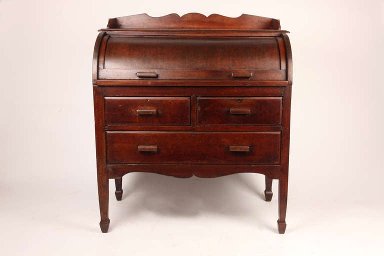 This Burmese teakwood desk serves a dual purpose as both a place for writing, as well as storage. The curved solid wood cover slides back to reveal cubbyholes and a pull-out writing surface. With two side-by-side drawers above a single larger