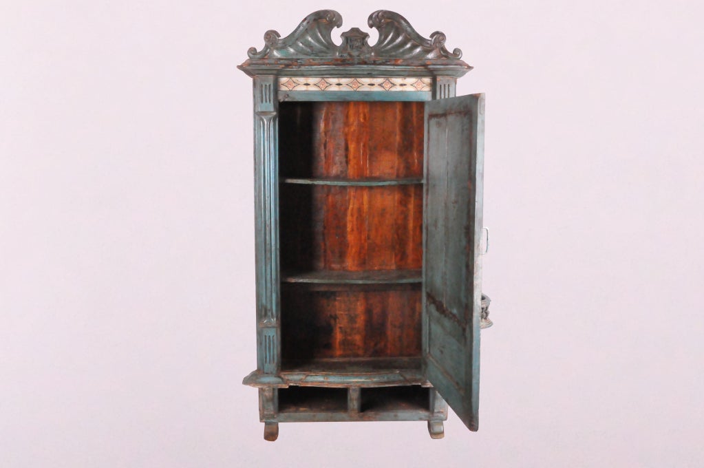 This painted Teak British Colonial cabinet is a good example of an Anglo-Indian hybrid. The form and decoration of the piece is British. The bright blue paint was probably added later and reflects Indian cultural preferences. The earlier layer