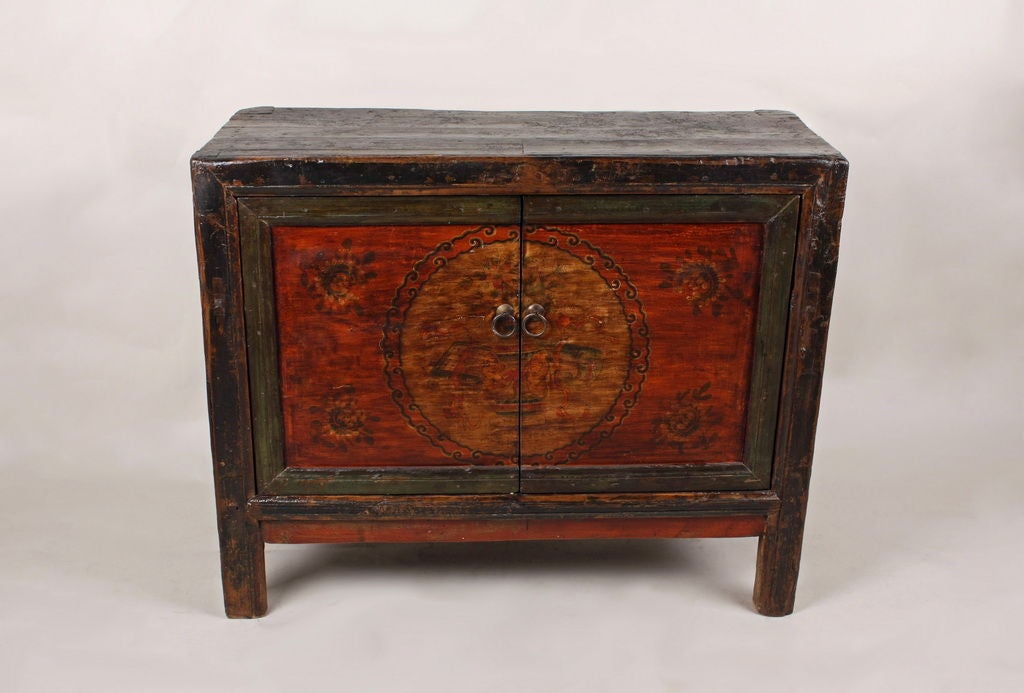 Elevated tibetan Chest with painted front. Prodominet coloring red and dark green and black, depicting floral designs.  Internal storage with single shelf, dual cabinet door opening.