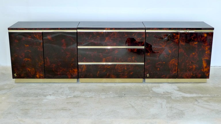 Sumptuous three chest console clad in faux tortoiseshell with brass pulls and accents from France, 1970's.  Outer sections are two door cabinets each with a single adjustable shelf. Middle section is three drawer small chest of three