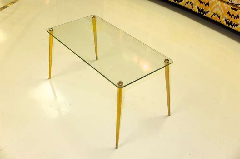 Simple and spare, recalling the Italian designs of Fontana Arte, this petite mid-century French low table consists of four brass tapered legs with brass capped tops which insert into four holes in the rectangular glass top.