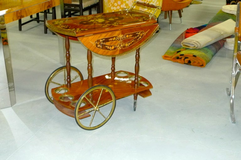 1960's Italian bar cart or tea trolley by Sorrento with elaborate inlaid marquetry on herringbone veneer which has a high gloss clear coat.  The side wings can be latched up to create a large round circular serving tray, or hang freely from their