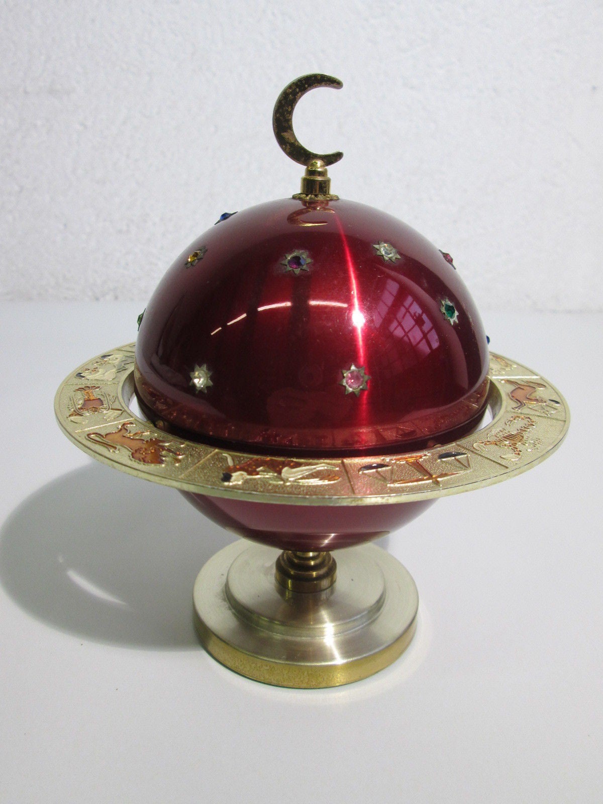 Vintage Italian cigarette holder in form a planet or globe which is red anodized aluminum and encrusted with jewels and surrounded by a Saturn-like ring decorated with Zodiacal figures, topped with a crescent moon finial. The top half of the globe