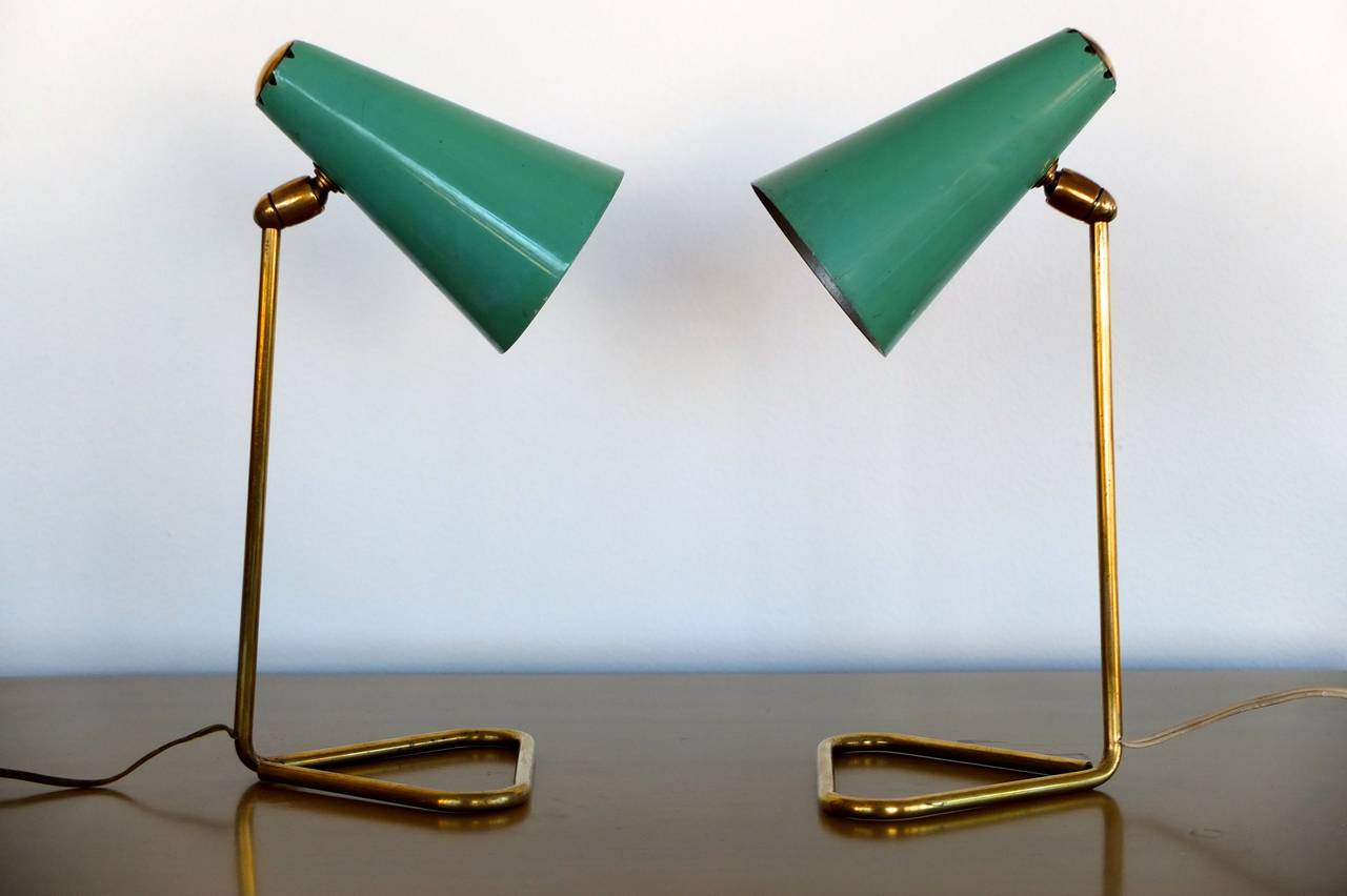 Versatile pair of lamps with brass triangle bases and swiveling cones in original sea foam green enamel. Cones swivel 360 and 180 degrees. Can be used as a wall lamp with a hook. Each takes a single candelabra screw cap bulb or mini spot up to 60
