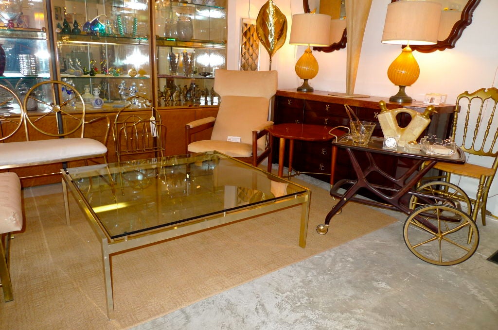 Clean simple Bauhaus modernist lines on this glass top square cocktail table constructed from a brass-finished aluminum frame.  Glass top rests on 3 posts on side flanks giving it a further air of lightness.<br />
<br />
Purchased in Toronto in