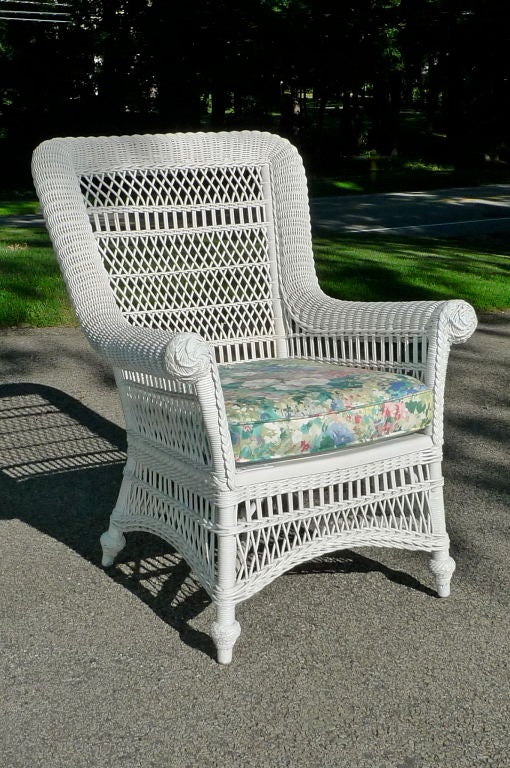 Feel the summer breeze and waft the perfumed wisteria frommthe comfort of this sturdy antique white wicker arm chair with a single foam cushion upholstered in floral chintz.