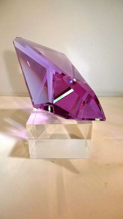 Unsigned artisan cut wedge of magenta colored glass resting on lucite cube base.