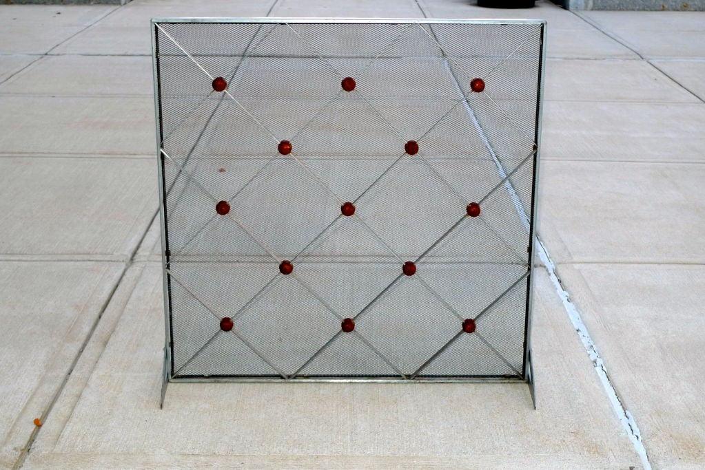 Intriguing standing fireplace screen; steel frame with cris cross metal grid forming a diamond pattern joined with rusted iron elements behind wire mesh.  The screen stands on its own with the support of two loosely hinged flat triangular brackets
